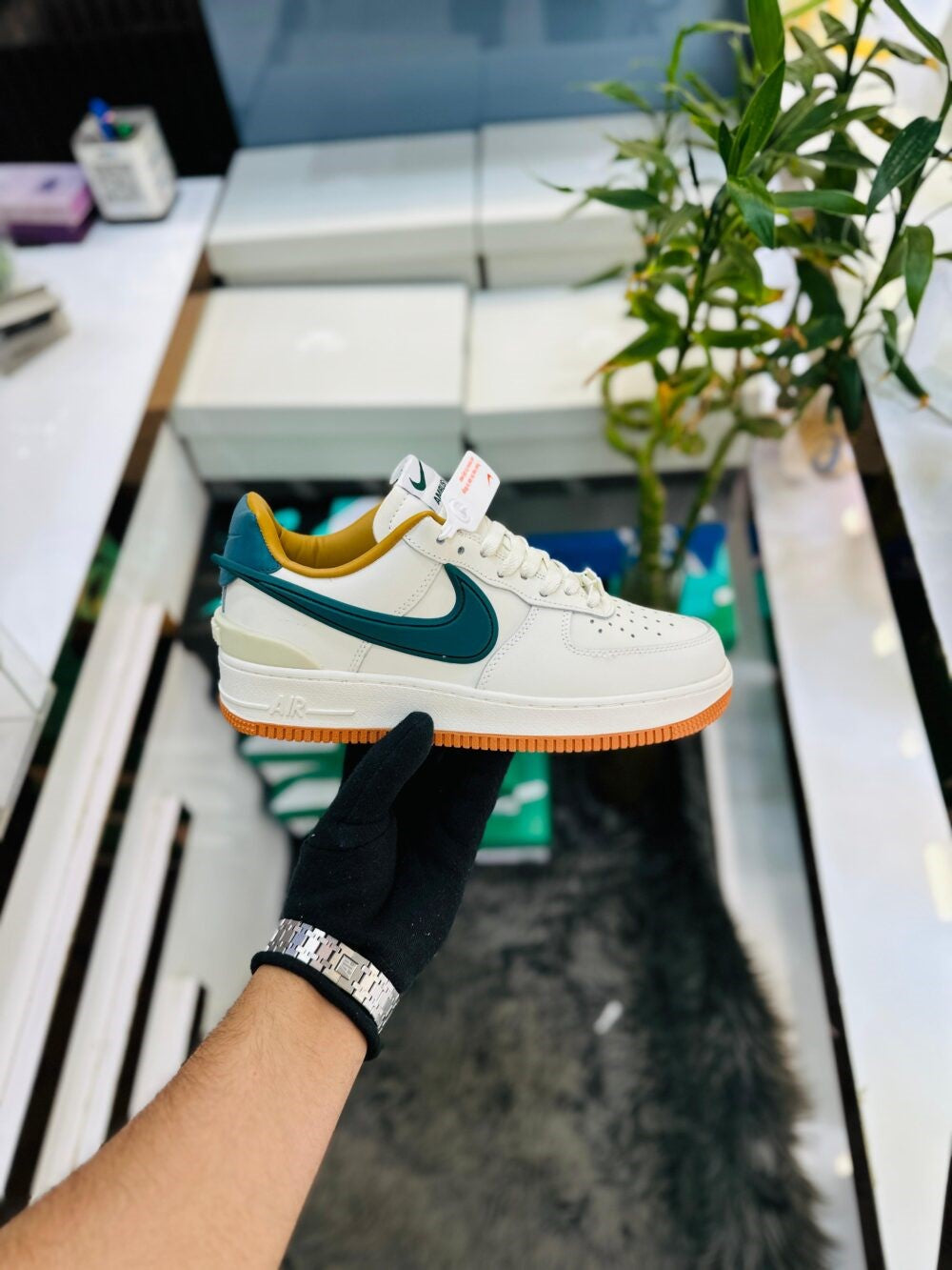 AMBHUS X NIKE AIR FORCE 1 LOW white sneaker with teal swoosh and mustard inner lining held in hand